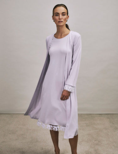 Woman wearing a light purple dress with a matching cardigan against a plain background